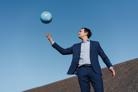 Mature businessman throwing a globe on a disused mine tip