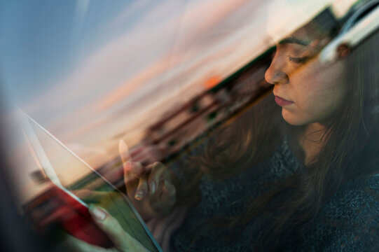 Young woman using digital tablet while travelling in car seen through glass window