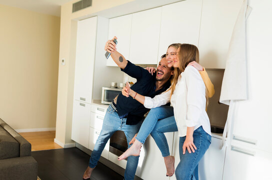 Friends having fun standing in the kitchen, taking pictures with their smartphones