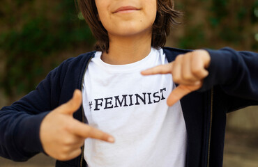 Fototapeta na wymiar Little boy standing in the street with print on t-shirt, saying Feminist, making finger frame