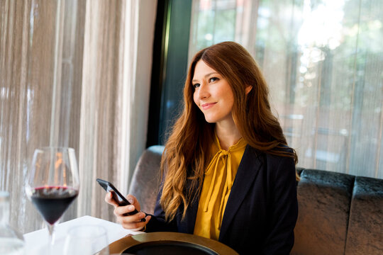 Smiling woman sitting at table in a restaurant holding cell phone