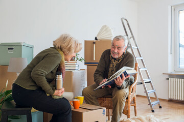 Senior couple looking at photo album surrounded by cardboard boxes in an empty room