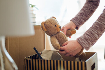 Close-up of woman unpacking cardboard box in new home taking out teddy bear