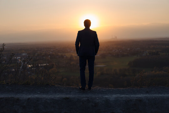 Mature businessman standing on a disused mine tip at sunset looking at view