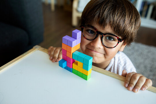 Portrait of smiling little boy with glasses playing with building blocks at home