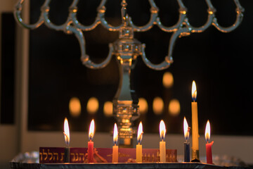 Colorful Hanukkah candles are lit, against a black background of the night - the Jewish holiday of...