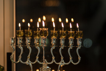 Hanukkah candles are lit in a silver-decorated menorah, against a black background of the night -...