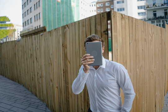 Businessman at a boarding in the city covering his face with a tablet