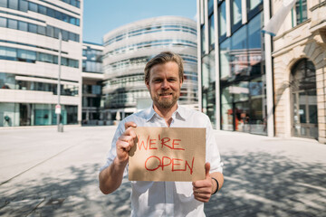 Shopkeeper holding cardboard with opening announcement in the city