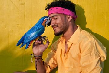 Young black man posing with a parrot in front of a yellow wall