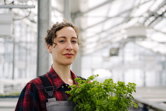 Portrait of confident woman with parsley plant in greenhouse of a gardening shop