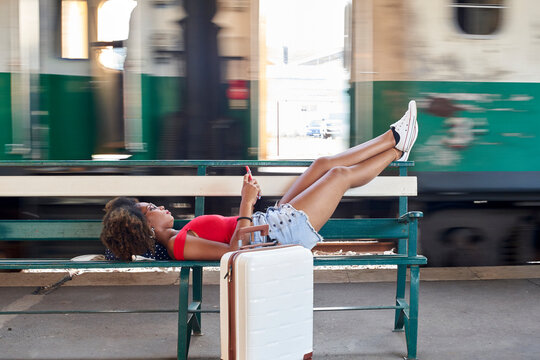 Woman with suitcase lying on a bench at the train station
