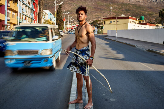 Tribal man with his traditional arch and arrows in the middle of the city with cars passing by, Lubango, Angola