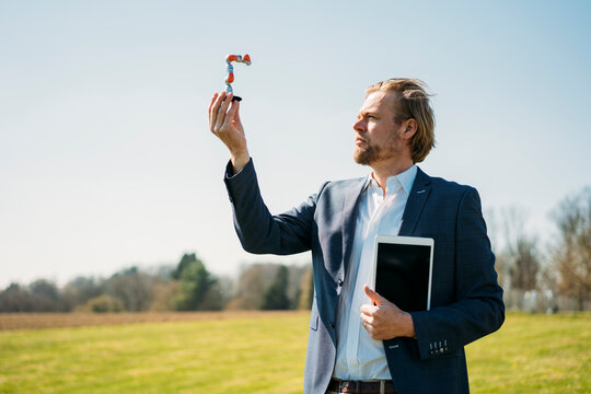 Businessman analyzing at small robotic arm while holding digital tablet against clear sky during sunny day