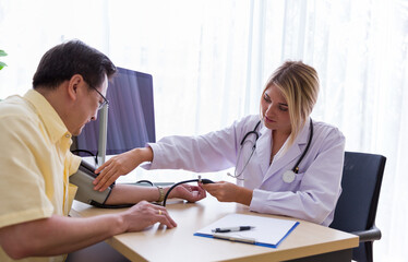 Fototapeta premium Female doctor using blood pressure gauge with senior male patient while sitting on the chair in the office at the hospital