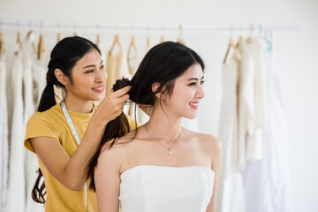 Attractive asian young bride is smiling in wedding dress with women assistant in wedding salon.