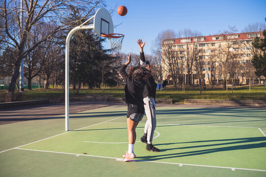 Young man and woman playing basketball on court