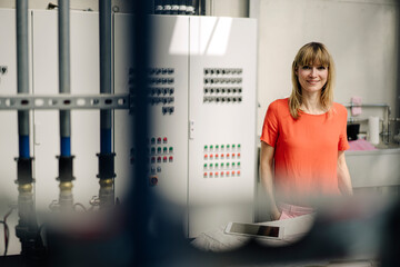 Smiling female entrepreneur standing against control panel in greenhouse