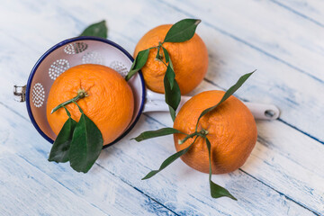 Three oranges with leaves and a colander on wood