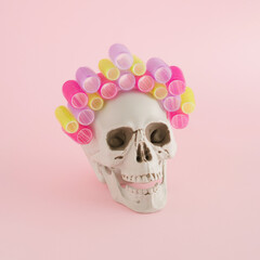 A creative arrangement  made of skull and curlers on a pink background. Minimal Halloween concept. Salon, hairstyle and beauty Inspiration.