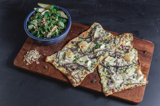 Tarte Flambee with camembert and thyme creme fraiche and red onion on chopping board, lamb's lettuce with pear in bowl