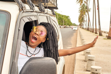Portrait of screaming woman with dreadlocks leaning out of car window, Maputo, Mozambique