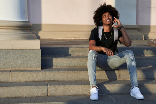 Young smiling man listening to music and sitting on steps