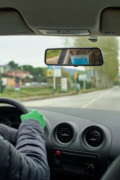 Man wearing mask and gloves driving car reflecting on rear-view mirror in city