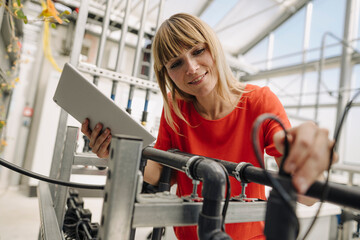Close-up of female entrepreneur holding digital tablet examining irrigation equipment