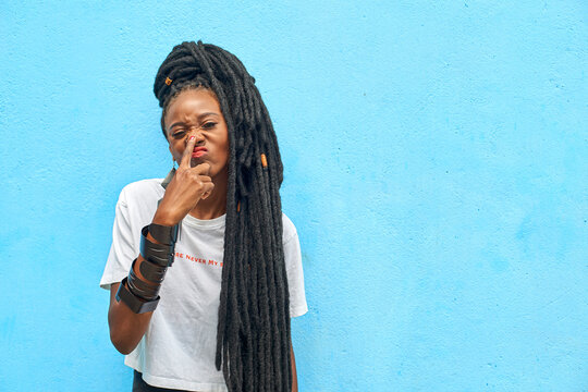 Portrait of woman with long dreadlocks touching her nose in front of turquoise wall