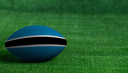 American football ball  with Botswana flag on green grass background, close up