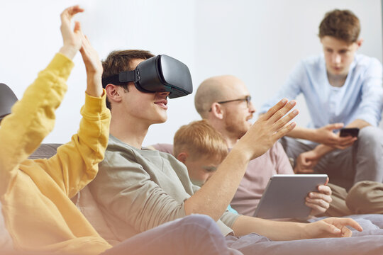 Happy family sitting on couch, using VR goggles and mobile devices
