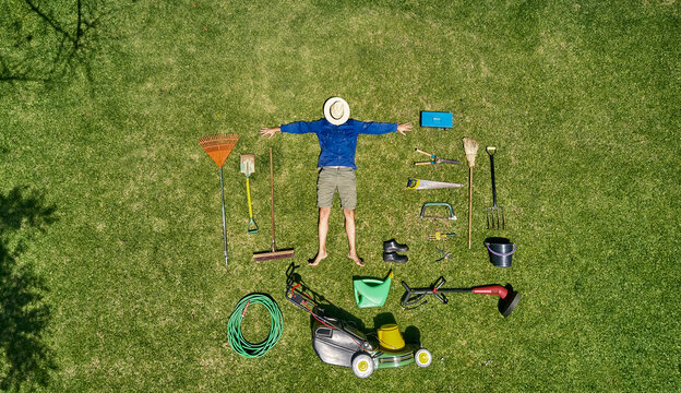 View from above of a gardener with sun hat on his face, laying on the grass with all the tools he need for take care of garden