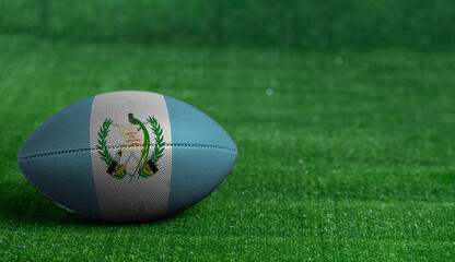 American football ball  with Guatemala flag on green grass background, close up