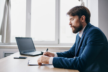 Fototapeta na wymiar bearded man sitting at a desk in front of a laptop finance technologies