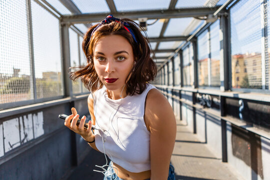Portrait of young woman with earbuds and cell phone on a bridge