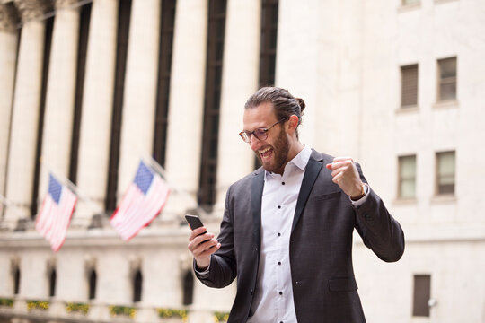 Excited young businessman looking at cell phone in front of Stock Exchange, New York City, USA