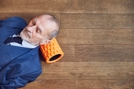 Senior businessman relaxing on wooden floor, resting on fascia roll