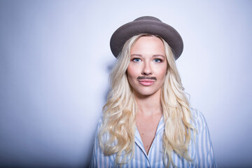 Portrait of blond young woman with fake moustache and hat