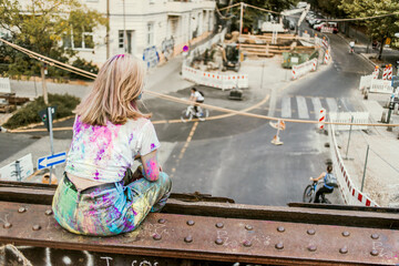 Girl with Holi colours on her clothes sitting on bridge, Germany