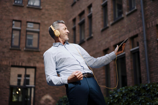 Carefree businessman dancing while listening music against building