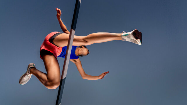 Worm's eye view of female runner crossing hurdle