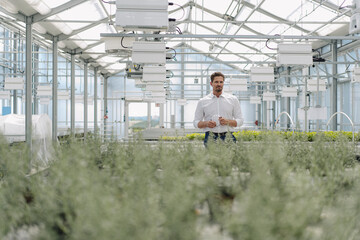 Male entrepreneur standing amidst plants while working in greenhouse