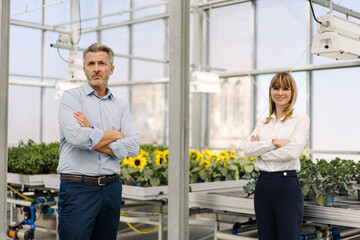 Confident male and female professionals with arms crossed standing in greenhouse