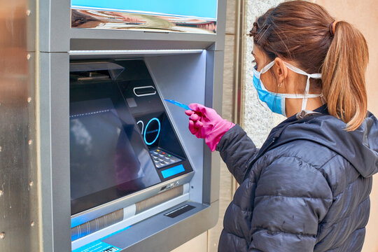 Woman wearing mask using credit card at ATM during pandemic situation