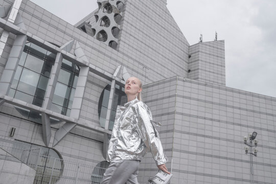 Cool girl in silver suit carrying VR goggles in a futuristic city