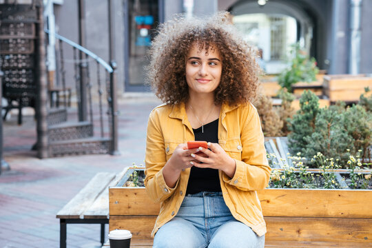 Portrait of smiling teenage girl sitting on bench with coffee and mobile phone
