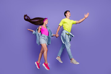 Fototapeta na wymiar Profile photo of dreamy youngster couple jump hold hands wear pin-up outfit isolated violet color background