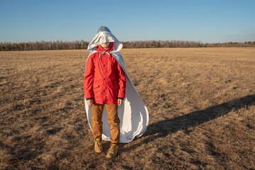 Hood of superhero costume covering boy's face in steppe landscape