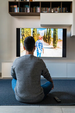 Back view of man sitting on the floor at home watching television
